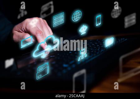 Person using a laptop keyboard, glowing cloud icons, data symbols, and network connections in a dark background. Concept of online storage Stock Photo