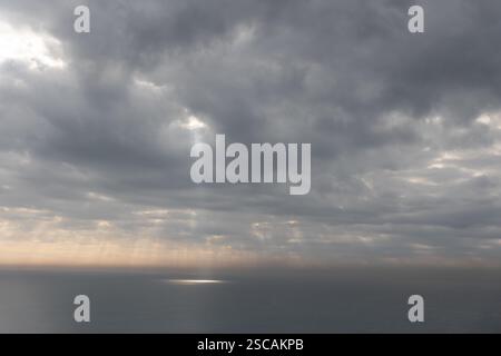 The sun rays breaking through gray clouds reflecting on the sea surface Stock Photo