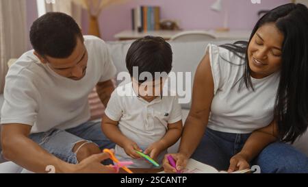 Latin family, including a man, woman, and child, enjoying quality time together indoors cutting paper with scissors in their cozy living room. Stock Photo