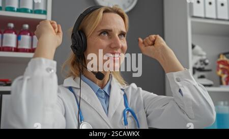 Woman doctor celebrating successful diagnosis in a modern clinic setting wearing a headset in a bright indoor hospital office. Stock Photo