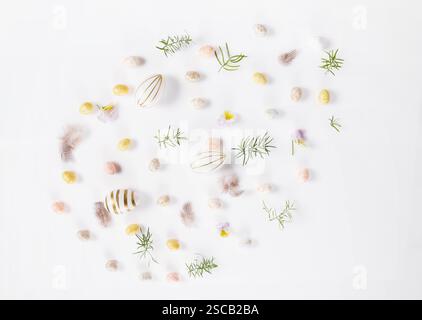 Minimalist Easter flat lay featuring elegant decorations: wooden bunnies, speckled eggs, soft feathers. Composition in shape of Easter egg on white Stock Photo