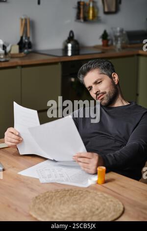 A handsome man studies printed papers at a well arranged kitchen table. Stock Photo