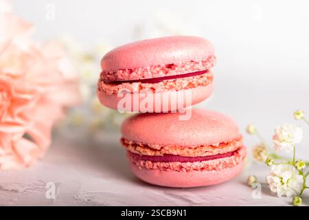 Two pink macarons on top of each other with some pink and white flowers on a white background Stock Photo