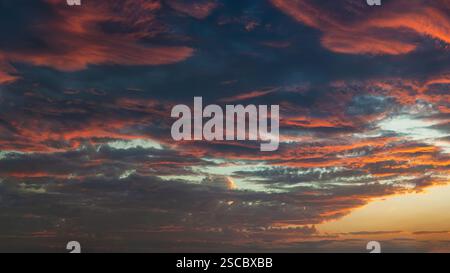 High-quality panoramic shot of the sky at sunset with contrasting warm and dark cloud layers. Stock Photo