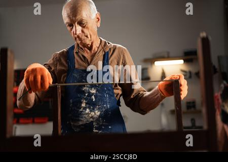Senior elderly man is taking measurements of an old chair using a tape measure. Carpentry workshop Stock Photo