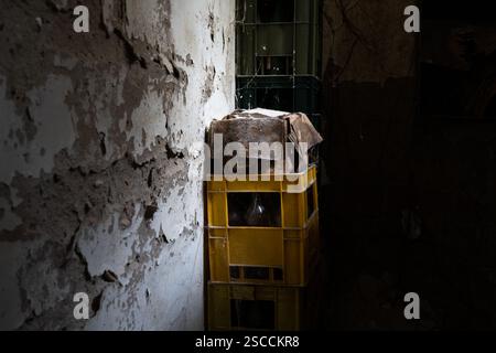 Plastic crates with bottles in abandoned storage room next to cracked wall illuminated with natural light through small window, urban exploration Stock Photo