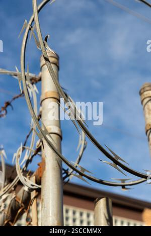 Razor wire on chain link fence with blue skies and clouds in the background. Stock Photo