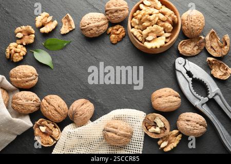 Frame of fresh ripe walnuts, shells and nutcracker on black table, flat lay Stock Photo