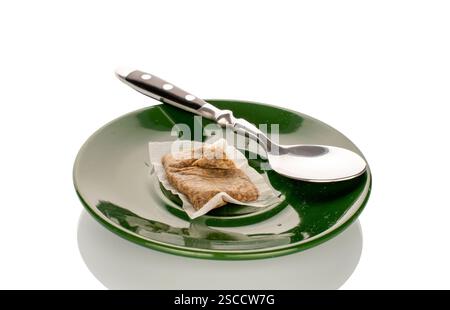 One used tea bag with a teaspoon on a ceramic saucer, close-up, isolated on a white background. Stock Photo