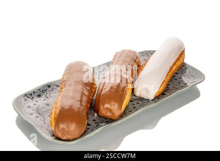 Three eclairs with cream filling on a ceramic saucer, close-up, isolated on a white background. Stock Photo