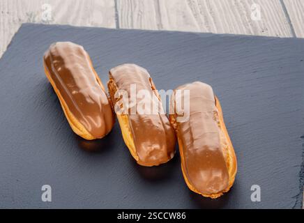 Three sweet eclairs on a slate stone, close-up. Stock Photo
