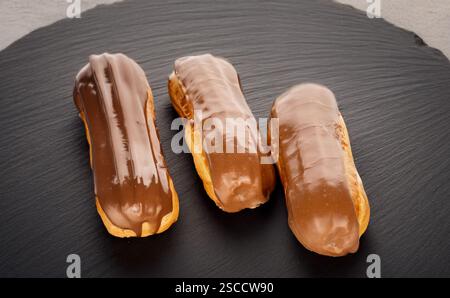 Three sweet eclairs on a slate stone, close-up. Stock Photo