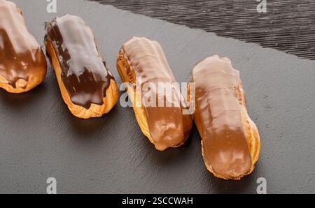 Three sweet eclairs on a slate stone, close-up. Stock Photo