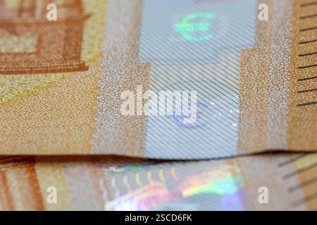 Close-up view of a Euro banknote, highlighting security features like iridescent foil and intricate patterned details in beige and white.  The focus i Stock Photo