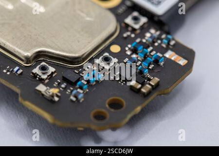 Close-up of a circuit board fragment, showcasing various components including a metallic element, surface-mount resistors, and small buttons. Predomin Stock Photo