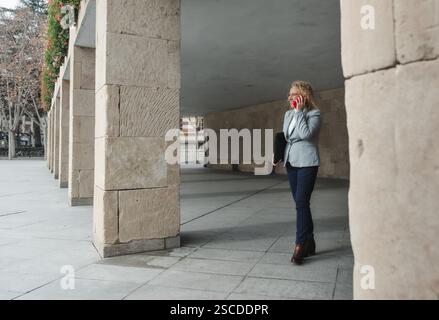 Businesswoman talking on phone while walking outdoors Stock Photo
