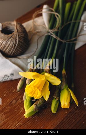 Daffodils on a wooden table on a sunny day indoors. Yellow narcissus or daffodil flowers. Spring flowers background. Spring card with place for text. Stock Photo