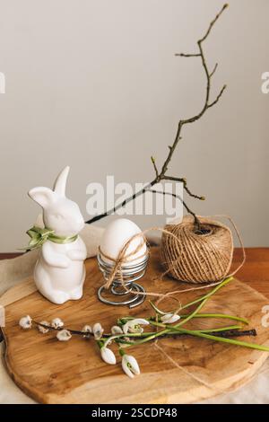 Spring composition with a white bunny, Easter egg and snowdrop flowers on a light background. Easter concept. Place for an inscription. Stock Photo
