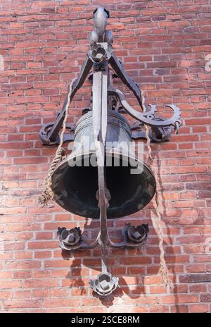 An ornate, weathered bell mounted on a brick wall, complemented by decorative metalwork and ropes Stock Photo