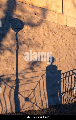 Shadow of street lamp and railing on a textured stone wall at sunset Stock Photo