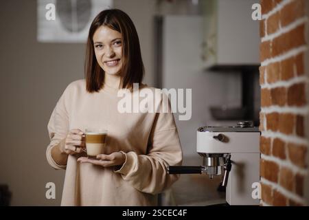 Woman holding a cup of coffee with an espresso machine in the background Stock Photo