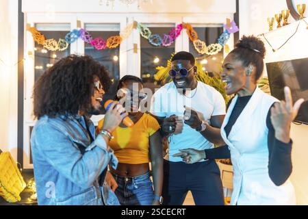 Latin man singing karaoke happily enjoying music with multi-ethnic friends at night home party Stock Photo