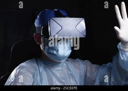 Individual in medical gear with a VR headset and a raised hand Stock Photo