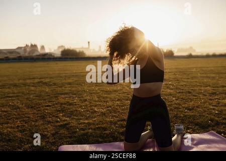 Woman adjusting hair while kneeling on a yoga mat in the sunlight Stock Photo