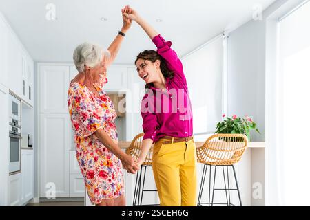 Beautiful grandmother and granddaughter together at home having fun while dancing in the apartment - Cheerful granma and nephew spending quality time Stock Photo