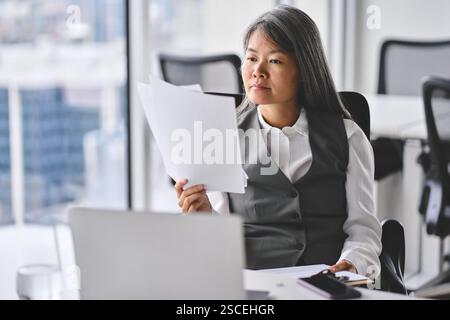 Busy older Asian business woman working in office reading document. Stock Photo