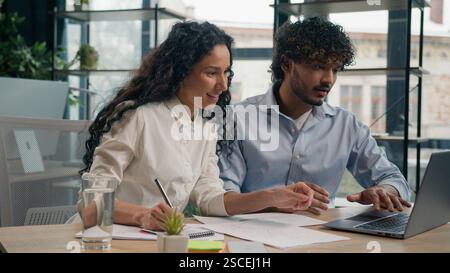 Arabian female employer insurance agent consult Indian male client discuss business project finance marketing data on laptop two multiracial Stock Photo