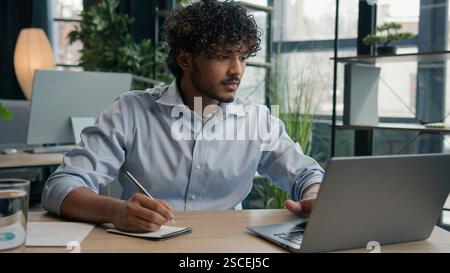 Indian Arabian man accountant writer business entrepreneur businessman write notes in notebook latino guy writing ideas report paperwork on office Stock Photo