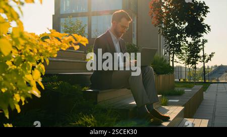 Businessman working with laptop in city successful male entrepreneur Caucasian guy man office executive ceo use computer on steps campus typing Stock Photo