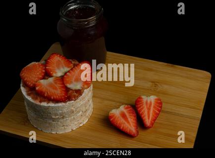 The rice cake with strawberries on top and a jar of jam next to it. One strawberry is cut in half and the strawberries are arranged in a heart shape Stock Photo