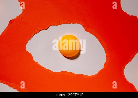 Eggs made of orange torn paper on a white background with ping pong balls. Abstract creative pattern Stock Photo