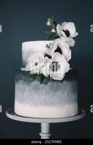 A beautifully crafted two-tier cake features a smooth ombre design in shades of gray. Elegant white flowers with dark centers adorn the cake, adding a Stock Photo
