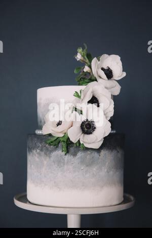 A beautifully crafted two-tier cake showcases a gradient design in soft gray tones, adorned with delicate white flowers, perfect for a memorable event Stock Photo