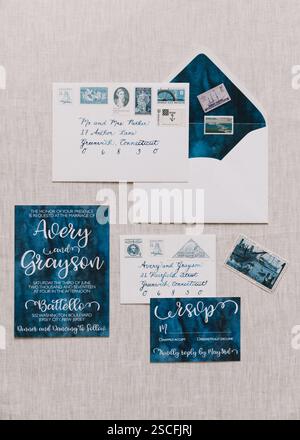 A beautifully arranged wedding invitation suite showcases hand-lettered designs, envelopes, and vintage postage stamps set against a neutral backdrop, Stock Photo