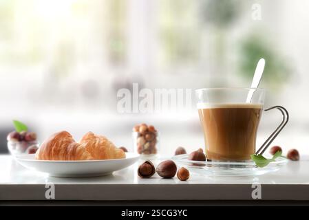 Cup of coffee with hazelnut drink and two croissants on a kitchen bench with fruits around it. Front view. Stock Photo