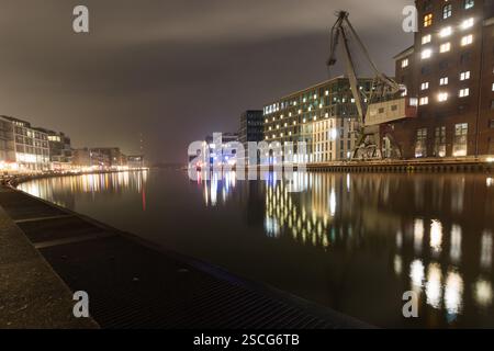 A serene nighttime view of the Münster harbor, featuring industrial and modern architecture reflecting beautifully on the calm water under a moody sky Stock Photo