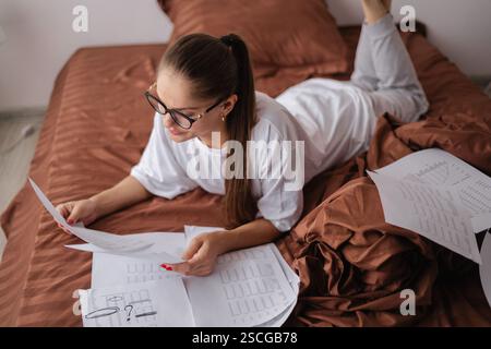 Accounting bookkeeping concept. Top view of woman in eyeglasses leading personal finances works at home working with papers on her bed Stock Photo