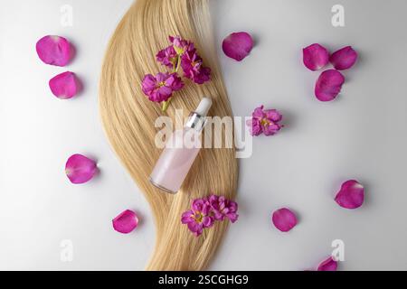 A pink face serum or oil made of rose petals with flower extract lying on a strand of blonde hair, product marketing mockup. A concept of hair care in Stock Photo
