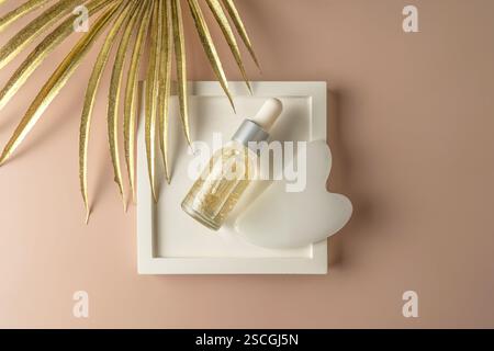 A natural transparent hyaluronic face serum with golden parts and a face massager in the form of the heart lying on a white ceramic plate Stock Photo