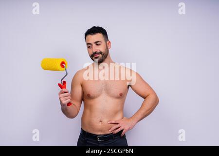 Young employee handyman using paint roller hold face isolated on background studio. Stock Photo