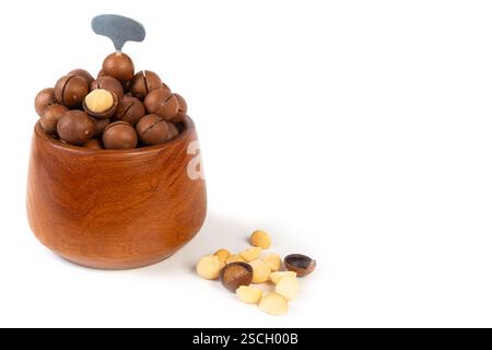 A wooden bowl filled with assorted macadamia nuts highlights their creamy texture and inviting look, with some scattered around. Stock Photo
