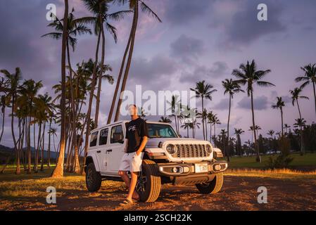 Man Standing by White Jeep Wrangler Among Palm Trees at Sunset Stock Photo
