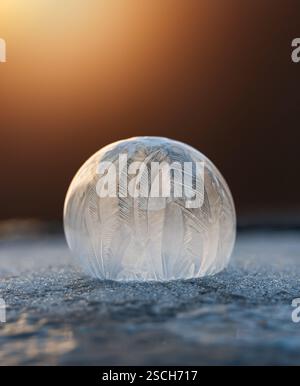 Close up of frozen soap bubble on snow with warm light behind it. Stock Photo