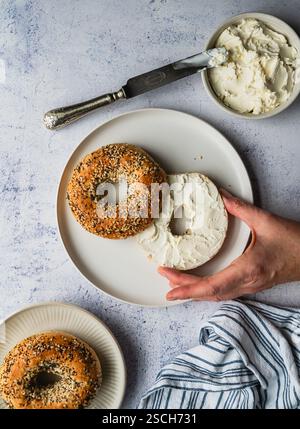 Top view of hand taking bagel with cream cheese off of a plate. Stock Photo