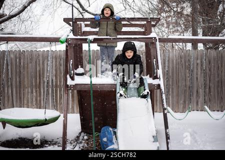 Two kids playing on snow covered slide and playset Stock Photo