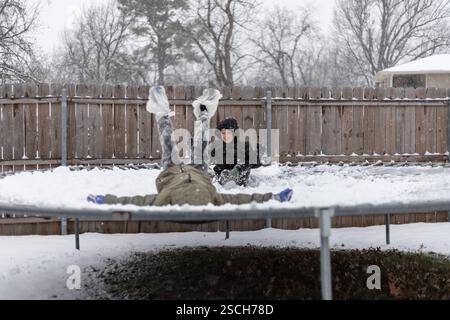 Two kids playing on a snow-covered trampoline in winter Stock Photo